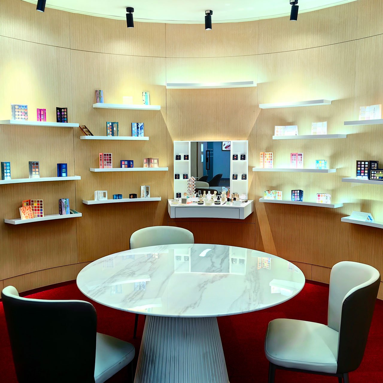 A showroom with a white marble-patterned round table, with shelves on the walls filled with various types of eyeshadows and palettes.