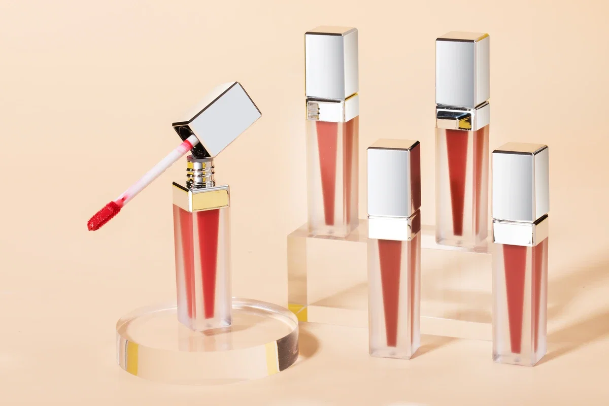 Five Soft Matte Lip Creams in various shades (magenta, nude, etc.) standing on acrylic columns. Light yellow background.