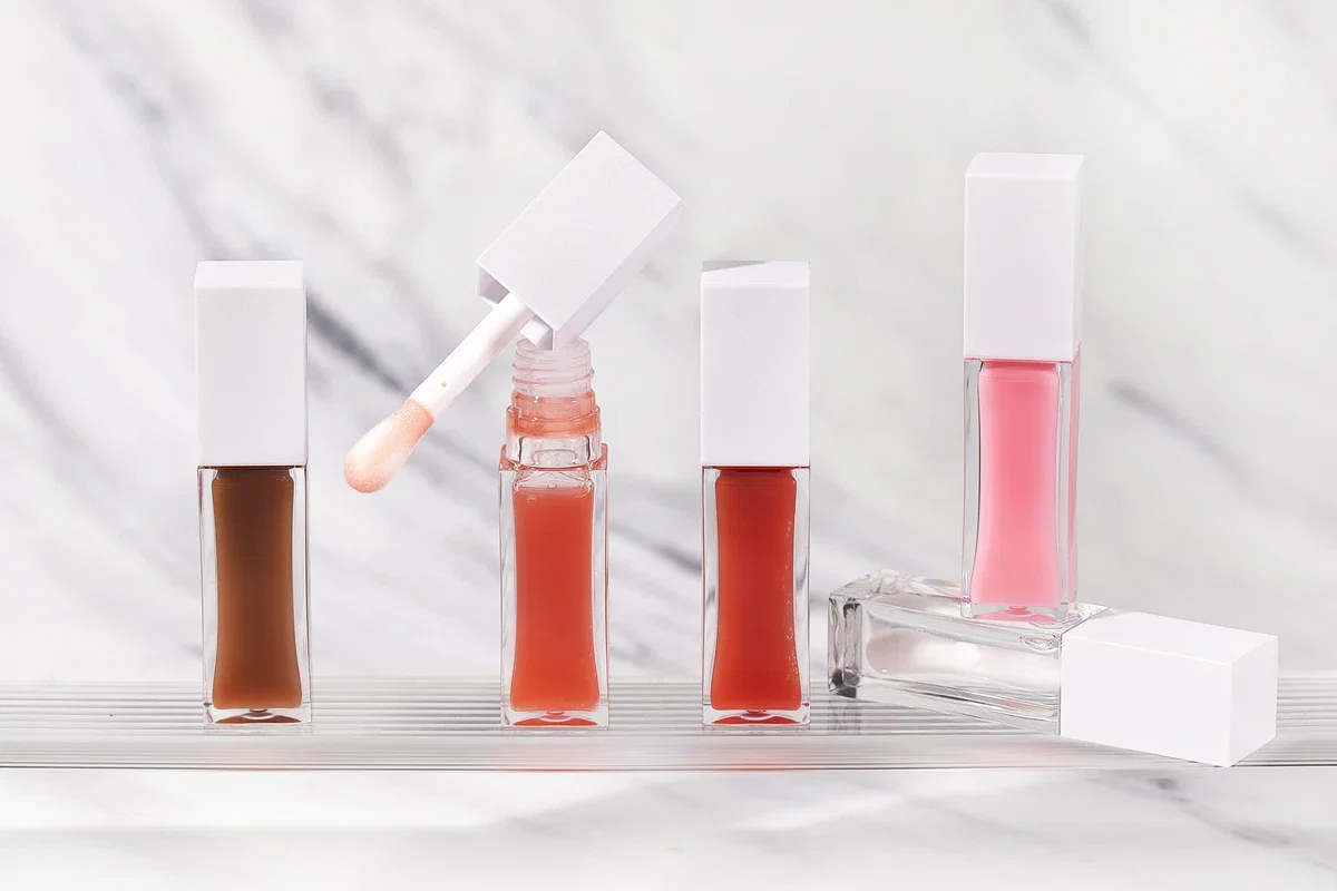 Close-up of private label lip gloss in peach and nude tones with square white tubes and marble-patterned background.