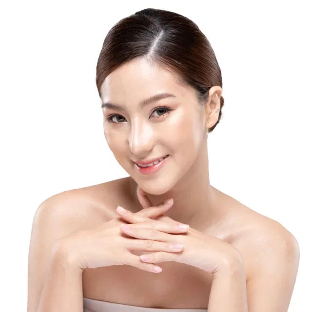 Красивая азиатская женщина с чистой кожей улыбается и прикасается к щеке на белом фоне